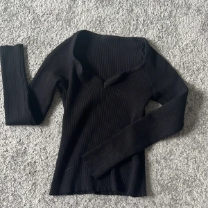 Svart ribbad långärmad tröja - Svart långärmad tröja med ribbad struktur och v-ringad hals. Sitter snyggt och har en smickrande passform som funkar till många olika looks. Perfekt att styla med jeans eller kjol för en clean vibe.