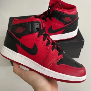 Nike Air Jordan 1 Mid Gym Red/Black - Säljer ett par Nike Air Jordan 1 Mid i färgen Gym Red/Black. Skorna har klassisk svart och röd färgblockning, vit mellansula och svart yttersula. Tillverkade i skinn med perforerad tå, svarta snören och ikoniska Jordan Wings-loggan på sidan. Pris kan diskuteras vid snabbaffär