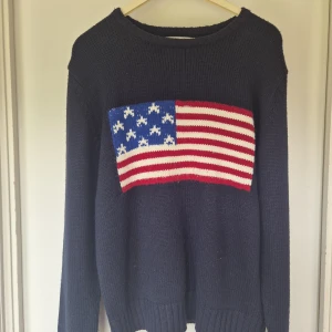 Mörkblå stickad tröja Brave Soul - Mörkblå stickad tröja från Brave Soul med amerikansk flagga i rött, vitt och blått på bröstet. Klassisk rund halsringning och långa ärmar. Perfekt för dig som vill sticka ut med en cool och casual look.