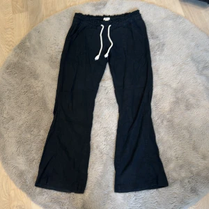 Svarta linnebyxor från Roxy med snörning - Svarta linnebyxor från Roxy med avslappnad passform och bootcut-ben. Byxorna har resår i midjan och vit snörning framtill för extra skön känsla. 