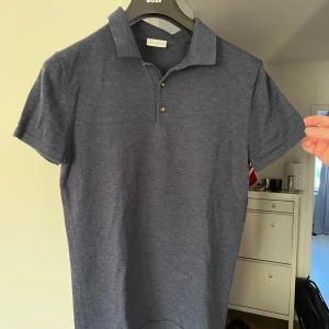 Mörkblå pikétröja i merinoull John Henric - Snygg mörkblå pikétröja från John Henric i 100% merinoull. Klassisk krage, tre knappar framtill och korta ärmar. Perfekt för dig som vill ha en stilren och bekväm tröja med exklusiv känsla. Passar till både jeans och chinos.