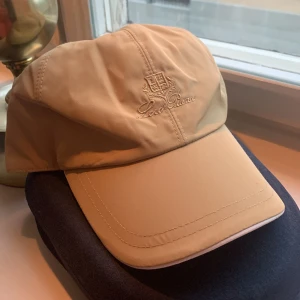 Loropiana beige keps (Diskutera om pris) - Beige Loropiana keps , Kepsen har broderad logga framtill, justerbar rem bak och insida i rutigt tyg. Materialet är vattenavvisande och känns lyxigt och stiligt på samma gång.