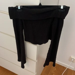 Svart ribbad offshoulder topp - Svart ribbad offshoulder topp från Shein i storlek XS. Toppen har långa ärmar och är tillverkad i väldigt mjukt material. Snygg croppad modell med bred kant upptill som sitter snyggt över axlarna.