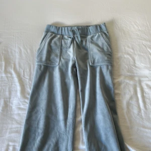 Blå mjukisbyxor Juicy Couture XS - Supermjuka ljusblå mjukisbyxor från Juicy Couture med bred resår i midjan och snörning. Byxorna har stora fickor fram och bak med knappdetaljer. Perfekta för chill dagar och har en loose passform.