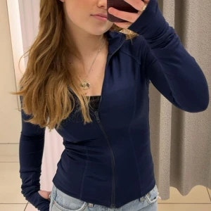 Mörkblå slim träningsjacka med dragkedja - Säljer en mörkblå slim träningsjacka med hel dragkedja framtill. Jackan har lång ärm med tumhål och hög krage. Snygg och sportig passform i stretchigt syntetmaterial, perfekt för aktiva dagar. Säljer pga jag tycker inte jag passar i mörkblå. Nästan helt oanvänd 