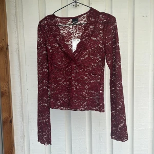 Vinröd spetsblus med v-ringning - Supersnygg vinröd blus från Gina Tricot i genombruten spets med v-ringning och långa ärmar. Blusen är figurnära och har ett romantiskt uttryck med blommigt spetsmönster. Perfekt att styla med jeans eller kjol för en trendig look.