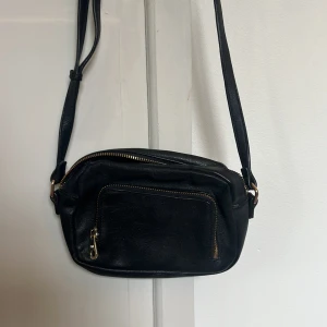 Svart axelväska i skinn från Don Donna - Svart axelväska i äkta skinn från Don Donna. Väskan har justerbar rem, guldfärgade dragkedjor och ett praktiskt ytterfack med dragkedja. Insidan har ett mindre fack med dragkedja för småsaker. Perfekt storlek för det viktigaste. Det är bara att skriva vid frågor. Pris går att diskutera!