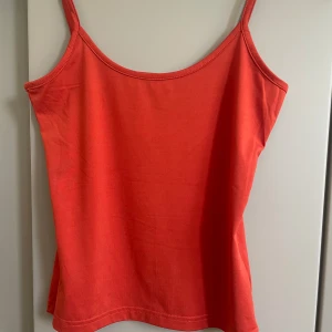 Röd /orange linnetopp från Lindex XS - En enkel och snygg röd/orange  linnetopp från Lindex i storlek XS. Toppen har smala axelband och rak passform, perfekt för varma dagar. Tillverkad i mjuk bomull som känns skön mot huden. Stilren och lätt att matcha med jeans eller kjol.