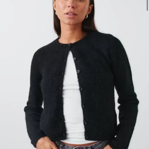 Svart kofta i ull från Gina Tricot - Mysig svart kofta från Gina Tricot i ullblandning. Klassisk rund halsringning, knäppning framtill med svarta knappar och lång ärm. Perfekt att slänga över en t-shirt eller linne för en chill look. Använd en gång så den är i nytt skick. 