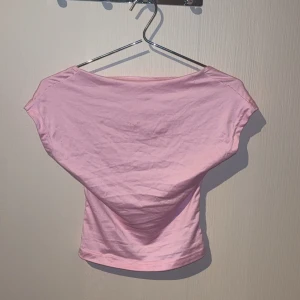 Ljusrosa topp med öppen rygg - Säljer en ljusrosa topp i mjuk bomull med korta ärmar och en riktigt snygg öppen rygg. Toppen är croppad och har en enkel, clean look framtill. Perfekt för dig som vill ha något stilrent men ändå vågat.
