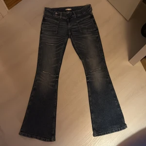 Mörkblå bootcut jeans med slitningar - Snygga mörkblå jeans med bootcut passform och slitningar på framsidan. Jeansen har stora framfickor och klassiska bakfickor. Materialet är jeans i bomull och de har en lågmidjad design. Perfekta för dig som gillar en retro vibe.