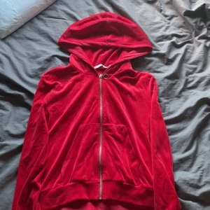 Röd velourhoodie från 157 med dragkedja - Riktigt snygg röd hoodie i mjuk velour från 157. Tröjan har huva, hel dragkedja med ringdetalj och en stor magficka framtill. Perfekt för dig som gillar en chill och trendig stil. Passar lika bra till jeans som till mjukisbyxor. 