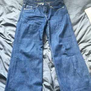 Blå wide jeans från Monki, 27/30 - Säljer ett par blå jeans från Monki i modellen wide leg. Klassisk femficksdesign, hög midja och raka, vida ben. Jeansen är i kraftig denim och har snygga kontrastsömmar. Perfekta för dig som gillar en avslappnad och trendig look.