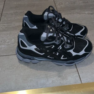 Asics gel nyc  - Snygga Asics gel nyc sneakers i svart och grått med coola detaljer och meshpaneler för extra andningsförmåga. Skorna har en chunky sula och klassisk snörning. Perfekta för dig som gillar sportig stil och vill ha bekväma skor till vardags. Tyvärr så följer ej Box med för att det originellt ej är mina skor och jag vet ej vad ägaren gjort av den, men skorna är fortfarande helt nya och oanvända. Pris kan såklart sänkas vid snabb affär. Storlek 40 men passar 39.