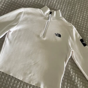 Vit half zip tröja från The North Face - Snygg vit långärmad tröja från The North Face med half zip och hög krage. Broderad logga på bröstet och patch på ärmen, croppad modell i mjuk bomull. Aldrig använd så är i nyskick!