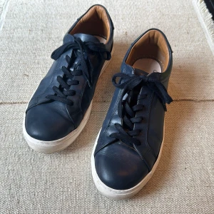 Mörkblå sneakers från Boggi i skinn - Snygga mörkblå sneakers från Boggi i mjukt skinn med vita platta sulor och svarta snören. Insidan är fodrad i beige läder för extra komfort. Klassisk och stilren design som passar till det mesta.