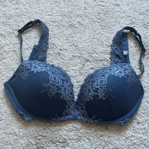 Intimissimi bh - Snygg mörkblå bh från intimissimi med vadderade kupor och breda axelband täckta av blommig spets. Kuporna har ett diskret blommönster och bh:n har justerbara axelband för perfekt passform. Perfekt för dig som gillar en feminin och stilren look. Använd någon enstaka gång men är så gott som ny.