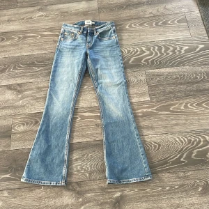 Blå bootcut jeans från 157, XXS - Snygga ljusblå bootcut jeans från 157 i storlek XXS Short. Klassisk femficksmodell med orangea sömmar och lätt slitning på låren. Jeansen har låg midja och är tillverkade i mjukt bomullsjeans-tyg. Perfekta för dig som gillar retrovibbar och utsvängda ben.