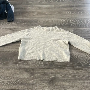 Ljusgrå stickad tröja från 157 - Mysig ljusgrå stickad tröja från 157 i storlek XS. Tröjan har en enkel och clean design med ribbade muddar vid hals, ärmslut och nederkant. Perfekt för lager-på-lager och chill dagar. Passar dig som gillar en avslappnad och stilren look.