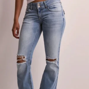 Ljusblå bootcut jeans med slitningar - Snygga ljusblå jeans med bootcut passform och slitna hål över knäna. Jeansen har klassisk femficksdesign, hög midja och är tillverkade i mjukt denimtyg. Perfekta för en avslappnad och trendig look.