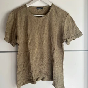 Beige mönstrad t-shirt från Lindex - Säljer en beige t-shirt från Lindex Basic i storlek 42/44. T-shirten har korta ärmar och ett diskret rutmönster i tyget som ger en snygg struktur. Perfekt för dig som gillar en enkel men ändå unik stil.
