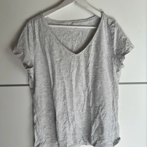 Ljusgrå v-ringad t-shirt - En basic ljusgrå t-shirt med v-ringning och korta ärmar. T-shirten har en avslappnad passform och är tillverkad i mjuk bomull, perfekt för en enkel och clean look. Passar till allt och är superenkel att styla.