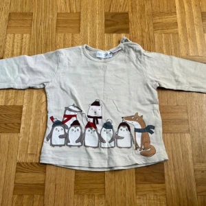 Beige långärmad tröja med djurmotiv Zara - Supersöt beige långärmad tröja från Zara med tryck av pingviner, räv, björn och andra djur i mössor och halsdukar framtill. Mjuk bomullskvalitet och rund hals med knapp vid axeln för enkel påklädning. Perfekt för mysiga dagar!