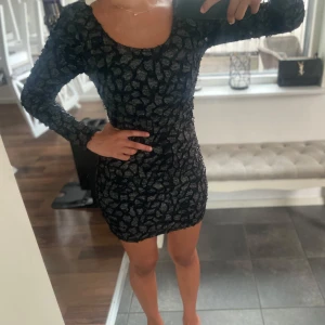 Svart och silvermönstrad  klänning - Supersnygg kort klänning med svart bas och glittrigt silvrigt mönster. Tight passform, långärmad och öppen rygg. Skriv för fler frågor