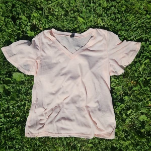 Ljusrosa v-ringad t-shirt från SHEIN - Säljer en ljusrosa t-shirt från SHEIN i storlek L, liten i storleken, mer som M. T-shirten har v-ringning och korta, lite fladdriga ärmar. Materialet känns lätt och luftigt, perfekt för varma dagar. Enkel och stilren design som är lätt att matcha med allt. Oanvänd då den var för liten.