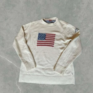Vit stickad Flag Gant tröja - Vit stickad tröja från Gant i bomull med broderad USA flagga på bröstet. Klassisk rund halsringning och ribbade muddar. Den är i storlek M och i superfint skick. Vid några frågor och funderingar är det bara att höra av sig.