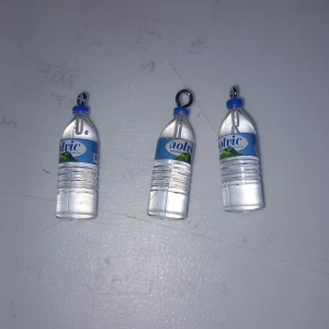 Vattenflaska örhängen i plast - Unika örhängen formade som små vattenflaskor med blått lock och etikett. Perfekt accessoar för dig som gillar roliga och annorlunda smycken. Tillverkade i transparent plast med blå detaljer och metallfäste för örat.