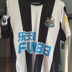 Newcastle United Isak 14 matchtröja S - Säljer en officiell Newcastle United fotbollströja med svarta och vita ränder, korta ärmar och klubbmärke på bröstet. Tryck med Isak och nummer 14 på ryggen. Premier League-märke på ärmen och sponsorlogga framtill. Perfekt för fans av Alexander Isak.