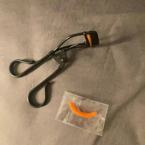 Svart ögonfransböjare LH cosmetics - Säljer en svart ögonfransböjare från LH cosmetics med orange silikonpad och extra refill. Böjaren är i metall med ergonomiska handtag och passar perfekt för att ge fransarna en snygg böj. Enkel att använda och stilren design.