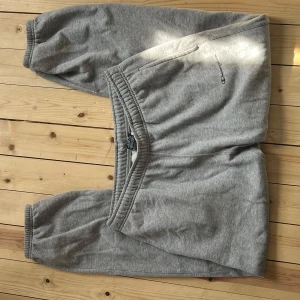 Grå mjukisbyxor från Champion M - Grå mjukisbyxor från Champion i storlek medium. Byxorna har resår i midjan och vid bensluten, samt sidofickor. Broderad Champion-logga på ena benet. Perfekta för chill eller träning, tillverkade i mjukt bomullsmaterial.