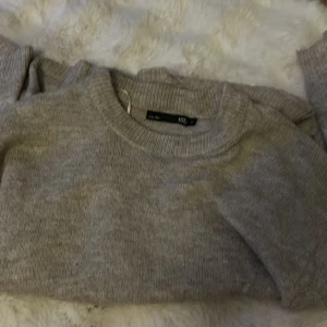 Grå stickad tröja från lager 157 - Mysig grå stickad tröja från 157 med rund halsringning och långa ärmar. Perfekt för lager-på-lager och chill dagar. Enkel och stilren design som funkar till det mesta. Materialet är mjukt och skönt mot huden. 