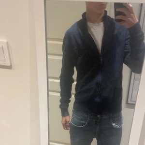 Mörkblå stickad kofta med dragkedja - Säljer en mörkblå stickad kofta med dragkedja framtill. Tröjan har hög krage och långärmad passform, perfekt för lager-på-lager. Enkel och stilren design som funkar till jeans.