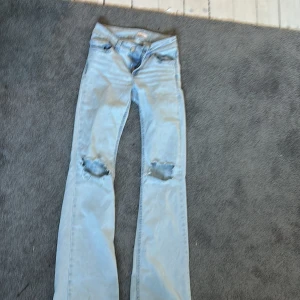 Bootcut ljusblå jeans från Nelly - Snygga ljusblå bootcut jeans från Nelly med slitna hål på knäna och coola röda broderade detaljer på bakfickorna. Jeansen har klassisk femficksdesign och är tillverkade i jeansmaterial med en skön passform. Perfekt för dig som gillar en avslappnad och trendig stil. Har en liten gul fläck som man inte märker av när man har på sig de men därav priset. Inte jätte använda bara några fåtal gånger max 10