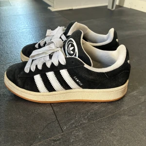 Adidas Campus svarta sneakers - Säljer ett par klassiska Adidas Campus sneakers i svart mocka med vita detaljer. De har använts men är fortfarande i fint skick. Inte slitna innuti, hela i hälen. Superfina! 