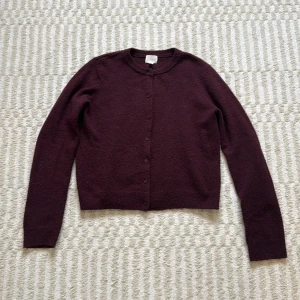 Vinröd/mörklila kofta från H&M - Mysig mörklila kofta från H&M i storlek M. Koftan har rund halsringning, långa ärmar och knäppning framtill med matchande knappar. Materialet är stickat och känns mjukt, perfekt till hösten🍂