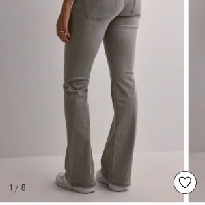 Grå bootcut jeans från Nelly - Snygga grå jeans från Nelly med låg midja och bootcut-ben. Jeansen har breda framfickor, dubbla knappar och dragkedja i gylfen. Materialet är klassisk denim i bomull och passformen är loose med en cool 00-tals vibe.