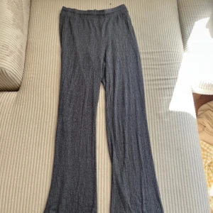 Grå ribbade byxor från Gina Tricot - Grå ribbade byxor från Gina Tricot i storlek S. Byxorna har en utsvängd passform med elastisk midja och är tillverkade i ett mjukt, stickat material. Perfekta för en chill och avslappnad look.