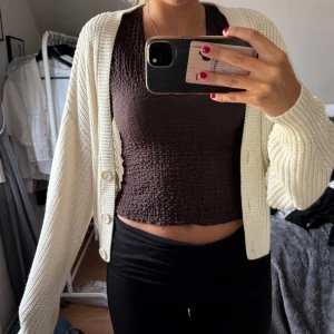 Vit stickad kofta från Divided - Säljer en krämvit stickad kofta från Divided med stora knappar framtill. Koftan har en loose passform, lång ärm och bred ribbad kant. Perfekt att slänga över en topp för en chill look. Superenkel att matcha och riktigt mysig.