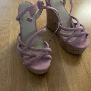 Rosa platåsandaler med korkklack - Snygga sandaler från ASOS med höga platåklackar i kork och remmar i ljusrosa mocka. Skorna har öppen tå och justerbart spänne vid ankeln. Perfekta för dig som vill sticka ut med en cool och trendig look.