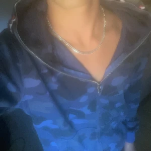 BAPE blå camo shark hoodie - Säljer en ikonisk BAPE shark hoodie i blå camo med dragkedja hela vägen och huva med broderade detaljer, tigrer och hajansikte. Tröjan har känguruficka och ribbade muddar. Perfekt statement-plagg för streetwear-stilen. Har änvändts få gånger bara. Jag är 181 och den är lite för liten på mig. Tveka inte på att höra av dig!