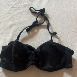 Svart bikiniöverdel från H&M, strl 36 - Snygg svart bikiniöverdel från H&M i storlek 36. Modellen har vadderade kupor, knytband i nacken och en söt rosett framtill. Perfekt för stranden eller poolen, enkel att matcha med olika underdelar.