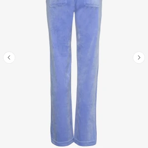 Blå velourbyxor från Juicy Couture - Snygga blå velourbyxor från Juicy Couture med broderad JC-logga på fickan. Byxorna har raka ben och bred resår i midjan för skön passform. Perfekt för dig som gillar den klassiska Y2K-stilen och vill ha något mjukt och chill. Obs: byxorna har ett ca 3 cm hål i sömmen till den främre högra fickan, detta fixas enkelt med nål och tråd. Mer än så är byxorna inprincipt oanvända och i mycket bra skick! 