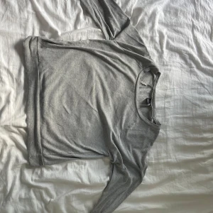 Grå basic tröja från Gina Tricot - Enkel och stilren grå långärmad tröja från Gina Tricot i mjuk bomullsmix. Tröjan har rund halsringning och normal passform, perfekt att matcha med jeans eller kjol. Snygg och clean look för alla tillfällen.