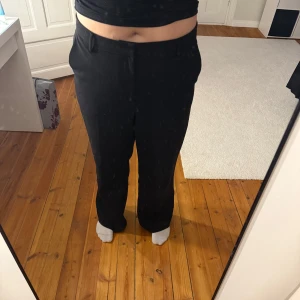 Svarta kostymbyxor med raka ben - Säljer ett par svarta kostymbyxor med raka ben och klassisk passform. Byxorna har hällor för bälte, snedställda fickor fram och fuskfickor bak. Perfekta för en clean och stilren look. Materialet känns mjukt och följsamt.