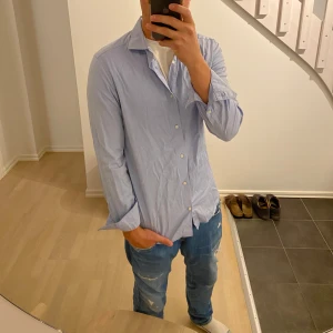 Ljusblå skjorta från Riley slim fit - Säljer en stilren ljusblå skjorta från Riley i slim fit-modell. Skjortan har klassisk krage, vita knappar och långa ärmar. Perfekt för dig som gillar en clean och enkel look. Materialet är mjukt och känns skönt mot huden.