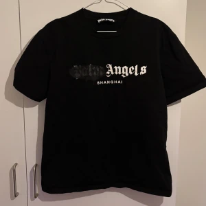 Svart Palm Angels t-shirt Shanghai - Svart t-shirt från Palm Angels med Shanghai-tryck i vitt och grått på bröstet. Klassisk rund hals och korta ärmar.